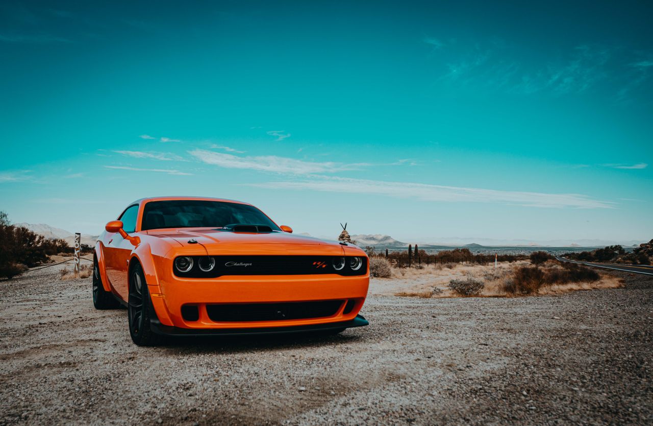 Orange Dodge Challenger sports car parked on a scenic Arizona desert road.